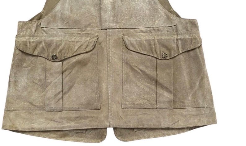 Peut inclure: Gros plan d'un gilet beige avec deux grandes poches avant et deux poches plus petites. Le gilet a un aspect vieilli, avec une texture visible et de l&eacute;g&egrave;res variations de couleur. Les poches sont fix&eacute;es par de petits boutons ronds.