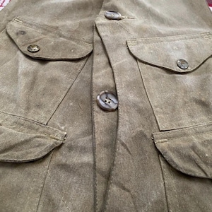 Peut inclure: Gros plan d'un gilet kaki avec quatre poches avant et de gros boutons ronds. Le gilet a un aspect l&eacute;g&egrave;rement us&eacute;, avec des coutures visibles et de subtiles variations de couleur du tissu. Les boutons sont de couleur marron clair.