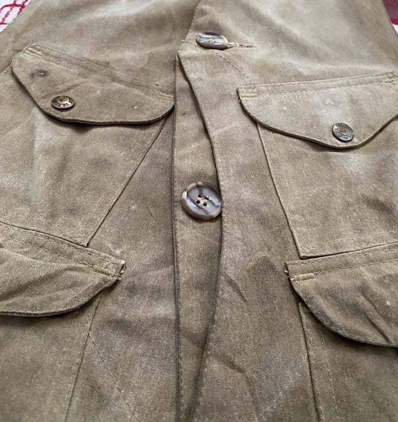 Peut inclure: Gros plan d'un gilet kaki avec quatre poches avant et de gros boutons ronds. Le gilet a un aspect l&eacute;g&egrave;rement us&eacute;, avec des coutures visibles et de subtiles variations de couleur du tissu. Les boutons sont de couleur marron clair.