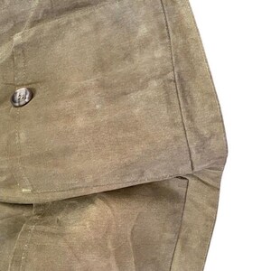 Peut inclure: Gros plan sur une section d'un sac en toile cir&eacute;e vert olive. Le sac pr&eacute;sente un grand rabat avec une fermeture &agrave; bouton. Le tissu a un aspect textur&eacute; avec de subtiles variations de tons.