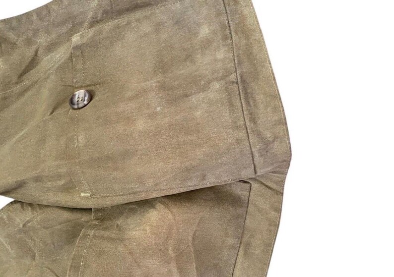 Peut inclure: Gros plan sur une section d'un sac en toile cir&eacute;e vert olive. Le sac pr&eacute;sente un grand rabat avec une fermeture &agrave; bouton. Le tissu a un aspect textur&eacute; avec de subtiles variations de tons.