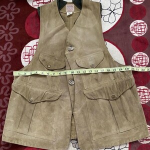 Peut inclure: Un gilet en daim beige avec quatre poches avant et des fermetures boutonn&eacute;es. Le gilet a un col vert fonc&eacute; et une &eacute;tiquette qui dit "FILSON". Le gilet mesure environ 51 cm de large au niveau de la poitrine.