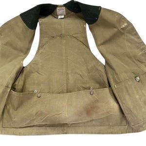 Peut inclure: Un gilet ouvert de couleur beige avec plusieurs poches et un col noir. Le gilet a un aspect us&eacute;, avec des coutures visibles et des fermetures &agrave; boutons m&eacute;talliques. Le design sugg&egrave;re un th&egrave;me de v&ecirc;tements de travail ou de plein air.