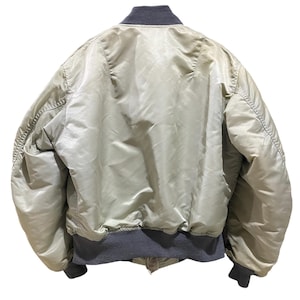 May include: Back view of a light green bomber jacket with a gray ribbed collar, cuffs, and hem. The jacket has a shiny, satin-like appearance and a classic bomber silhouette. The jacket is a neutral color.