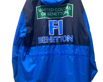 May include: A blue and navy jacket with a hood. The back of the jacket features the text "UNITED COLORS OF BENETTON" in white on a green rectangle, with "FI BENETTON" in blue below. The jacket is made of a lightweight material.