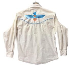 May include: White long-sleeved shirt with a button-down collar. The back has a blue and orange embroidered eagle design. The shirt features a curved yoke and buttoned cuffs. The shirt is hanging on a hanger.