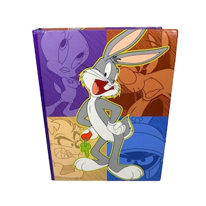 May include: A colorful box featuring Bugs Bunny with other Looney Tunes characters. The box has a square shape with a purple, orange, and blue background. Bugs Bunny is the central figure, with his mouth open and a carrot in his hand.