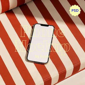 Puede incluir: Un smartphone con una pantalla blanca en blanco descansa sobre una superficie a rayas rojas y blancas. El teléfono tiene un borde negro y un marco dorado. El fondo presenta el texto "Phone Mockup by Lynie" y una insignia "PSD".