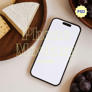 May include: A smartphone with a blank white screen is the focal point of this image, surrounded by wooden bowls filled with cheese and grapes. The words "Phone Mockup" and "by lyude" are overlaid on the image. A yellow flower-shaped sticker with the text "PSD" is also present.