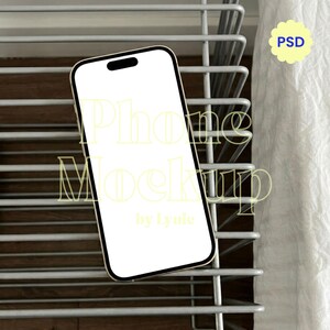 Może przedstawiać: Złoty mockup smartfona z pustym białym ekranem, spoczywający na szarej metalowej kratce. Ekran telefonu jest gotowy do personalizacji. Na ekranie wyświetlane są słowa "Phone Mockup" i "by lyuto". Naklejka "PSD" znajduje się w tle.