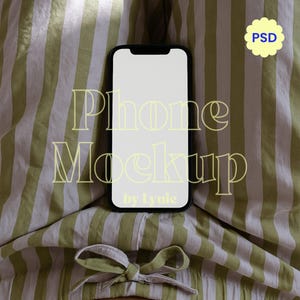 May include: A black smartphone with a blank white screen rests on striped green and white fabric. The text "Phone Mockup" is overlaid in a light yellow font, with "by Lyuie" below. A small yellow flower shape with "PSD" is in the upper right corner.