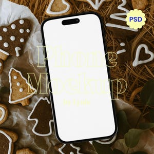 Może przedstawiać: Makieta smartfona z pustym białym ekranem, otoczona piernikami w różnych kształtach, w tym serc, gwiazd i drzew. Ciasteczka są ozdobione białym lukrem. Tło przedstawia suchą trawę i liście.
