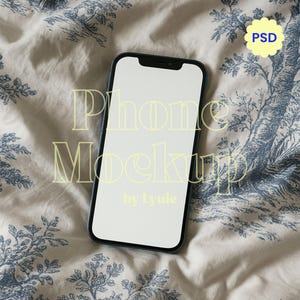 May include: A black smartphone with a blank white screen, positioned on a patterned fabric. The fabric features a blue and white floral design. Text on the image reads "Phone Mockup by lyuie" and a yellow "PSD" icon.