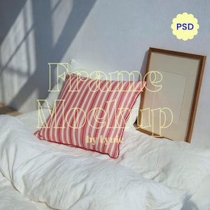 May include: A mockup scene featuring a bed with white linens, a striped red and white pillow, and a wooden picture frame. The text "Frame Mockup by Lyvie" is overlaid on the image, along with a "PSD" graphic.