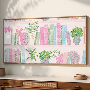 May include: A framed wall art print featuring a whimsical illustration of a bookshelf. The artwork showcases pink, green, and blue books, potted plants, and decorative bows. The print is set against a light pink background, creating a soft and inviting aesthetic.