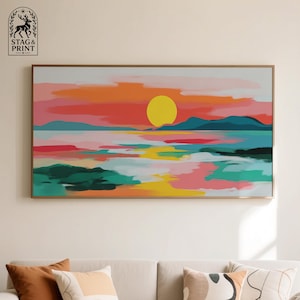 Peut inclure: Peinture de paysage abstrait représentant un coucher de soleil avec un grand soleil jaune, des nuages orange et roses, et des montagnes bleues. L'eau reflète les couleurs du ciel. L'œuvre encadrée est accrochée au-dessus d'un canapé.