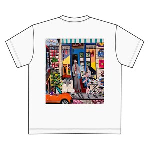 Könnte beinhalten: Ein weißes T-Shirt mit einer bunten Illustration einer Straßenszene mit einem Café, Menschen und einem Auto. Das Café hat ein Schild mit der Aufschrift "La Bavette".