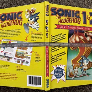 May include: A yellow "Sonic the Hedgehog 1 & 2" Sega's Official Player's Guide. The cover features Sonic and Tails, with the game's title in blue and red. The guide includes maps, tips, and special offers for merchandise.