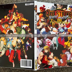 May include: A Street Fighter III Player's Guide book, featuring a collage of characters on the cover. The book has a black background with the title in a fiery font. The Capcom logo is visible.