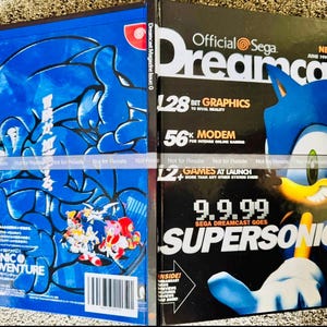 May include: A Sega Dreamcast magazine, issue 0 from June 1999, featuring Sonic the Hedgehog on the cover. The black cover displays the text 9.9.99 SEGA DREAMCAST GOES SUPERSONIC! and 128 BIT GRAPHICS. The blue back cover shows Sonic Adventure artwork.