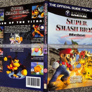 May include: A Super Smash Bros. Melee official strategy guide for the Nintendo GameCube. The front cover features Mario, Bowser, and Pikachu, while the back cover displays game screenshots, character art, and the text Smash of the Titans.
