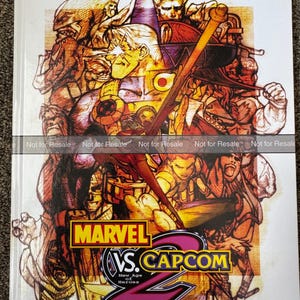May include: A Prima's Official Strategy Guide book for Marvel vs. Capcom 2. The cover features a collage of illustrated characters in shades of brown, yellow, and purple. The game's logo is prominently displayed with the Dreamcast logo in the bottom right corner.