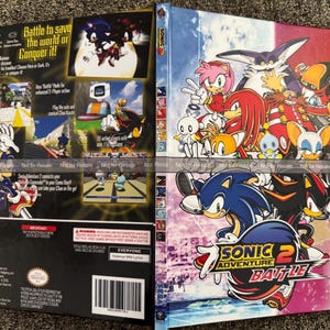 May include: A Sonic the Hedgehog video game case. The front cover features Sonic and Shadow, with the title "Sonic Adventure 2 Battle." The back shows gameplay screenshots and character art. The case is primarily blue, red, and white.