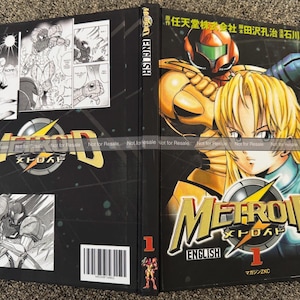 May include: A black and gold Metroid manga volume 1. The cover features a blonde woman and a character in a gold and orange suit. The title "Metroid" is in gold with a yellow lightning bolt. The back cover has black and white comic panels.