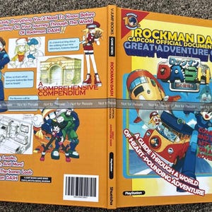 May include: An open Rockman DASH Capcom Official Documentation Great Adventure Guide book. The cover is orange with illustrations of characters and vehicles from the game. Text includes "A Comprehensive Compendium" and "A Guide Through a World of Heart-Pounding Adventure."
