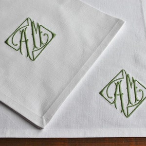 May include: Two white linen napkins with green embroidered initials "AM" in a diamond shape.