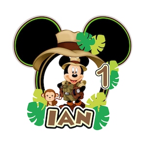 May include: A Mickey Mouse-themed birthday decoration featuring Mickey in safari attire, a monkey, the number 1, and the name "IAN". The design includes green leaves and a brown and tan color scheme, set against a white background.