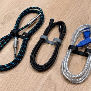 May include: Three coiled cables: one black and blue braided instrument cable with silver jacks, one solid black USB-C cable with a grey tie, and one translucent silver USB cable with a blue connector, each secured with a plastic cable tie.