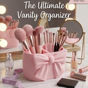 Könnte beinhalten: Ein rosa Schminktisch-Organizer in Schleifenform, gefüllt mit Make-up-Pinseln. Der Text "The Ultimate Vanity Organizer" wird angezeigt. Weitere Schönheitsprodukte, darunter ein Spiegel, eine Parfümflasche und Lippenstift, sind ebenfalls sichtbar.