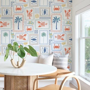 May include: A dining room with a white wall covered in a patterned wallpaper featuring crabs, fish, palm trees, lemons, and seashells. A round table with a white marble top and a woven base sits in front of the wallpaper. Two wooden chairs with tan leather seats are placed on either side of the table.