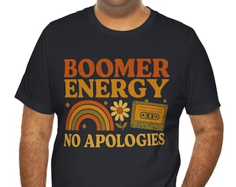 Puede incluir: Camiseta negra con el texto "BOOMER ENERGY NO APOLOGIES" en naranja y amarillo. El diseño incluye un arcoíris, una flor y una cinta de cassette en estilo retro.