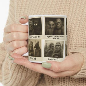 May include: White ceramic mug featuring vintage-style images of cryptids and extraterrestrials. The mug displays four panels with illustrations of Bigfoot, aliens, and other mysterious creatures, with text such as "Point Pleasant '87" and "Ireland '77".