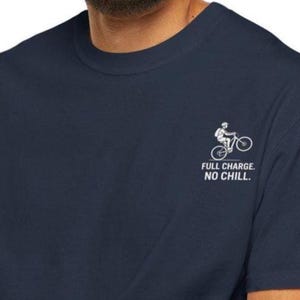 Puede incluir: Una camiseta azul marino con un gráfico blanco de una persona montando en bicicleta. El texto "FULL CHARGE. NO CHILL." está impreso debajo del gráfico.