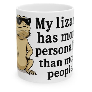 May include: White ceramic mug featuring a cartoon lizard wearing sunglasses. The mug has the text "My lizard has more personality than most people" in black, bold font. A fun gift for reptile lovers.