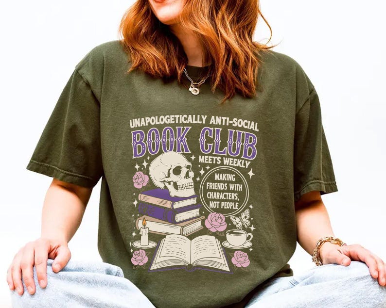 A person wearing a green t-shirt with a graphic design that says "Unaopoligically anti-social book club meets weekly" and includes a skull, books, and other symbols.