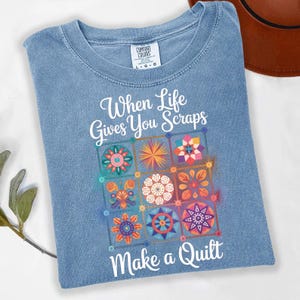 May include: A light blue Comfort Colors t-shirt with the text "When Life Gives You Scraps Make a Quilt." The shirt features a colorful quilt block design with floral and geometric patterns.