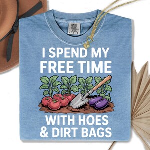 a blue t-shirt with a humorous text and an illustration of vegetables, including tomatoes and eggplants, along with a garden tool.