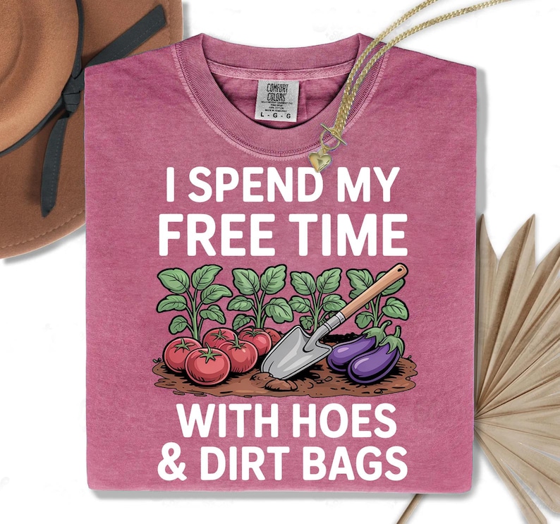 a pink t-shirt with a humorous text and an illustration of gardening tools and vegetables, including tomatoes, eggplants, and a shovel.