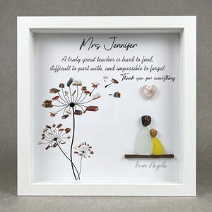 May include: White framed artwork with text "Mrs Jennifer" and a message about teachers. The artwork includes a dandelion design with books and a heart. A pebble art depiction of a teacher and student is also included.