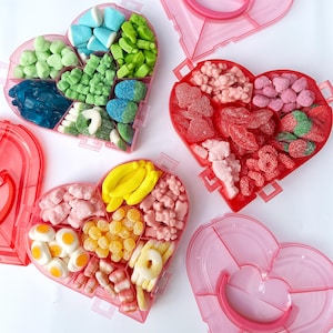 May include: Pink heart-shaped candy containers filled with a variety of colorful candies. The containers are divided into sections and have lids. Candies include gummy bears, jelly beans, and marshmallows.