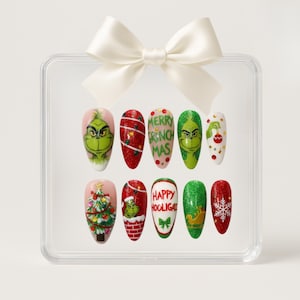 May include: A set of ten artificial nails featuring festive Christmas designs, including the Grinch, Christmas trees, and snowflakes. The nails are displayed in a clear box, tied with a white bow.