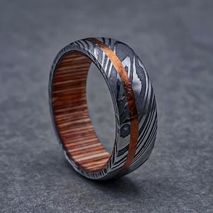 May include: A silver and copper patterned ring with a wooden inlay. The ring has a polished finish and a wide band.