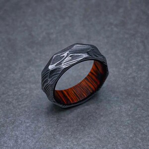 May include: A black and silver patterned ring with a dark wood inlay. The ring has a faceted design.