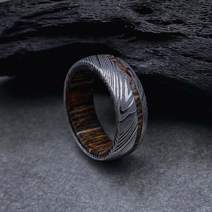 May include: A silver and brown patterned metal ring with a wood inlay.