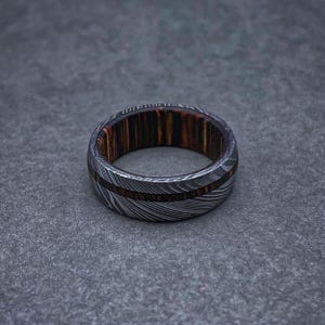 May include: A silver and brown patterned ring with a wooden inlay. The ring is made of metal and wood.