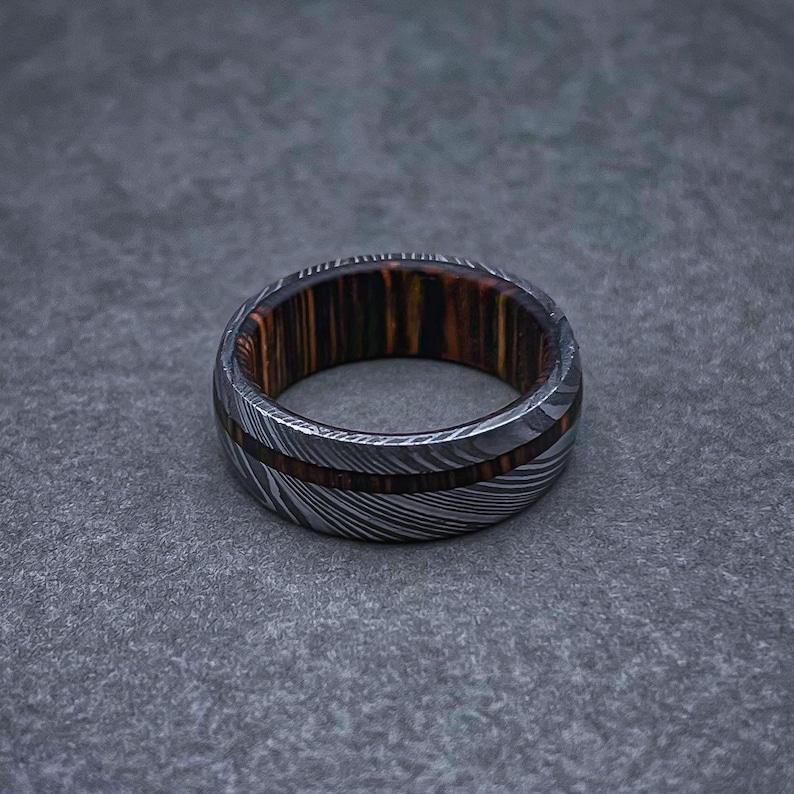 May include: A silver and brown patterned ring with a wooden inlay. The ring is made of metal and wood.